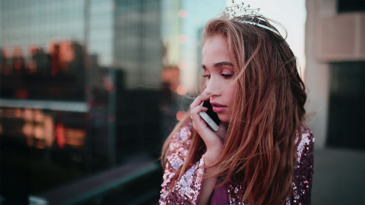 夜の電話占い：彼の本音や気持ちを知りたいと悩む女性が、都会の夜景を背景に携帯電話で相談する画像。当たる占い師で迷いをほどく。