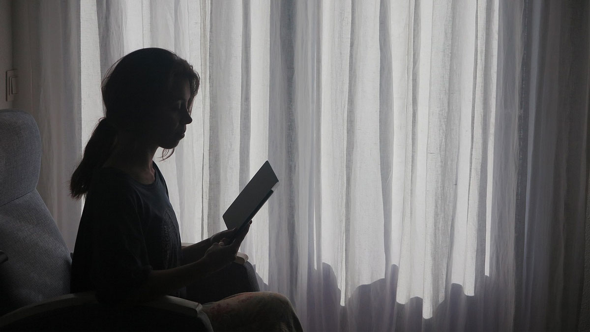 復縁のための冷却期間中、窓際で本を読み自己成長に努める女性のシルエット。耐えられない時の正しい過ごし方を解説